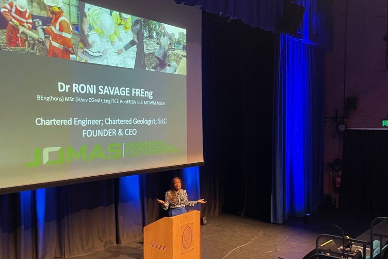 Dr Roni Savage behind a lectern, presenting.