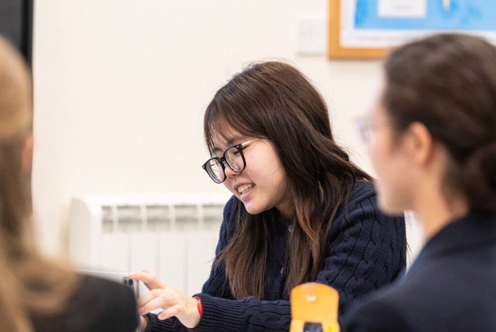 A pupils sat smiling, at her desk.